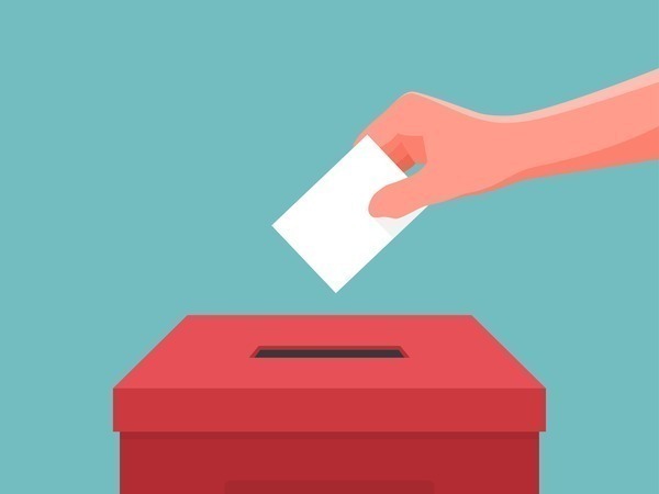 A hand posting a card into a ballot box