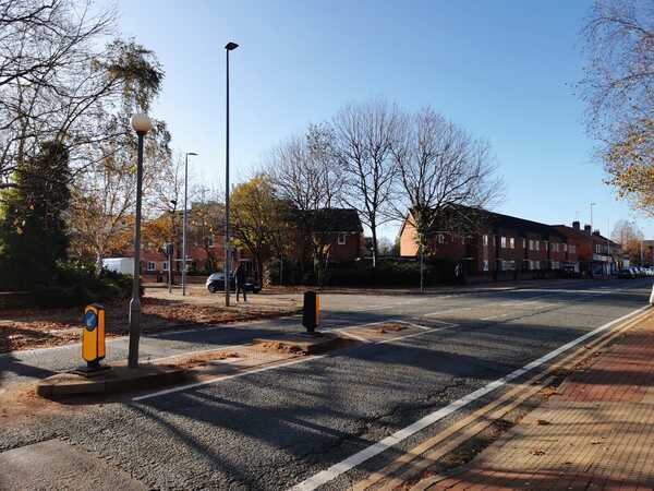 View down Eccles New Road at junction with Howard Street with a pedestrian crossing island in the middle and a row of houses in the background
