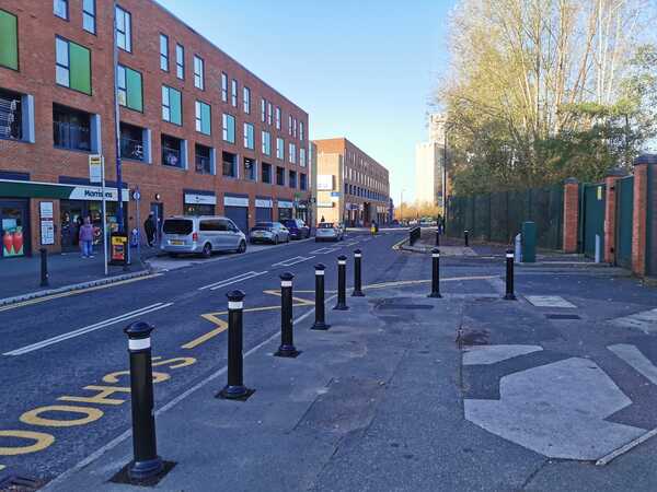 Looking down Phoebe Street outside Primrose Hill Primary School with shops on the left and bollards and fence on the right